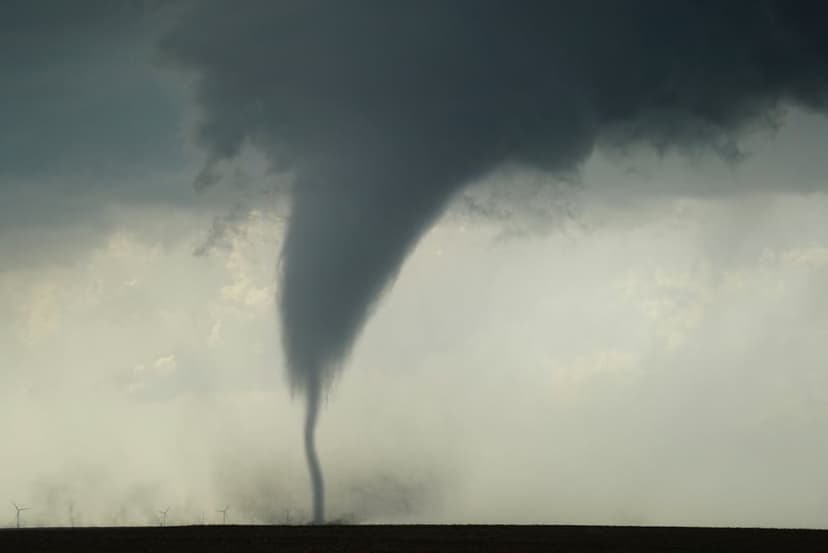 Dark tornado funnel cloud touching down on flat plains under a swirling grey and black stormy sky with debris.