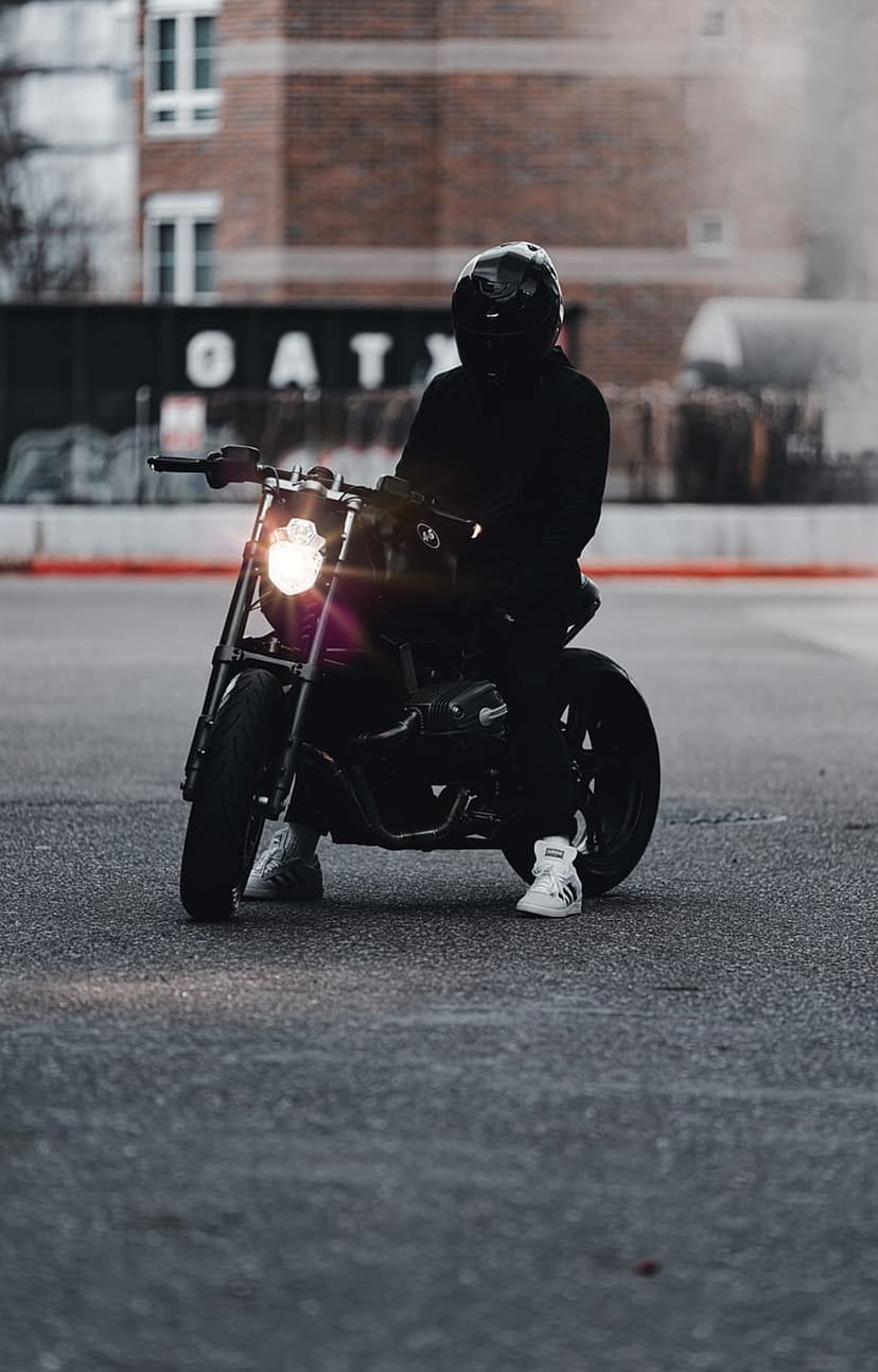 Biker in matte black gear sits on a dark motorcycle with a glowing headlight on a city street at night.