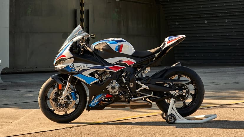 BMW S 1000 RR superbike in M Motorsport livery on a rear stand against an industrial hangar during sunset.