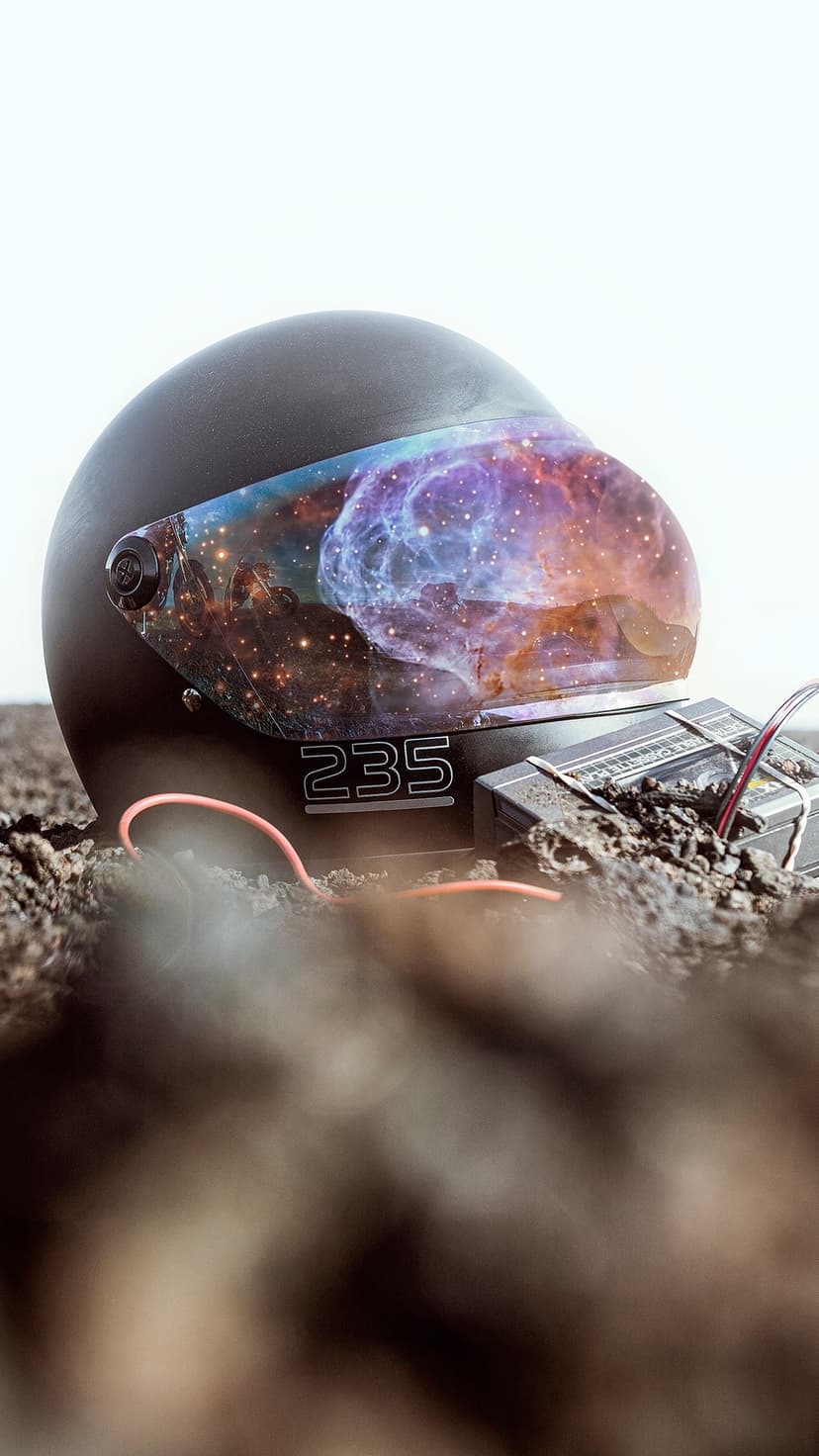 Matte black motorcycle helmet with a nebula-filled visor resting on earthy ground near a glowing pink wire.