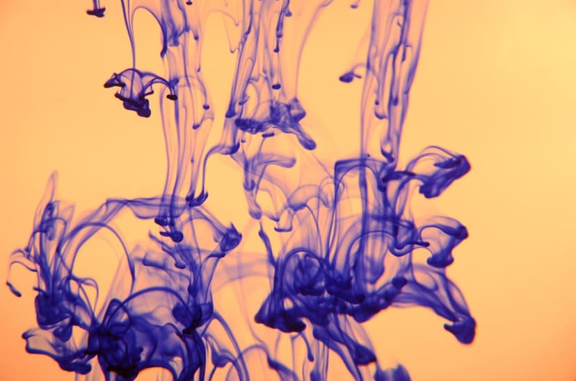 Deep blue ink clouds swirling in clear water against a glowing orange background with delicate fluid tendrils.