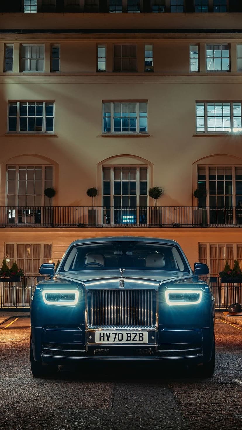 Rolls-Royce Phantom parked on a paved driveway before a glowing multi-story building during a quiet urban night.
