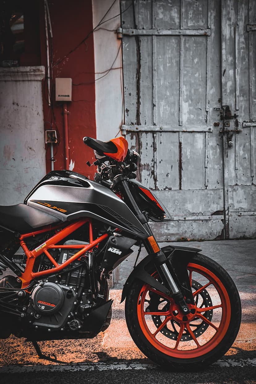 KTM Duke motorcycle with an orange frame parked before a weathered grey wooden door and a red striped wall.