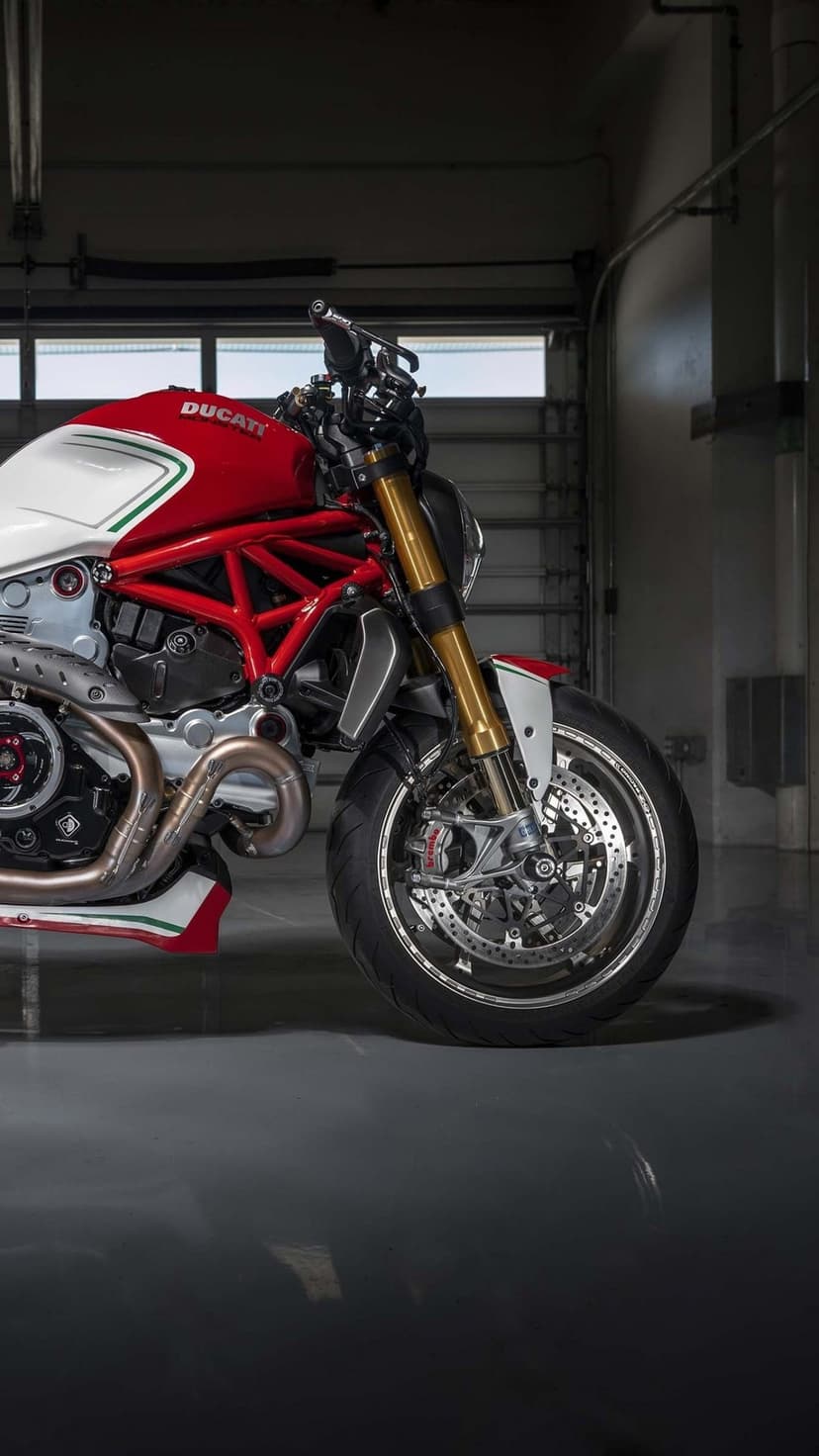 Red and white Ducati Monster motorcycle with gold forks and red frame in a modern industrial garage.