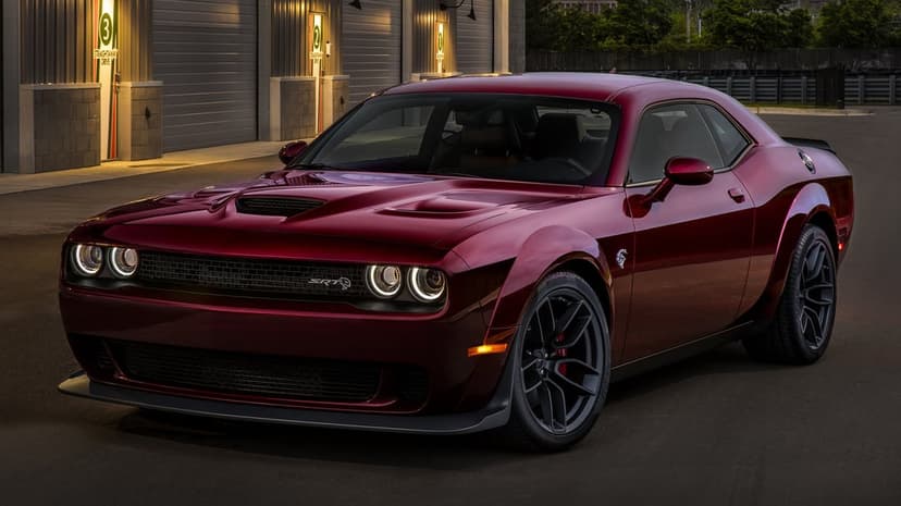 Maroon Dodge Challenger SRT Hellcat Widebody parked in front of industrial garage doors with evening lighting.