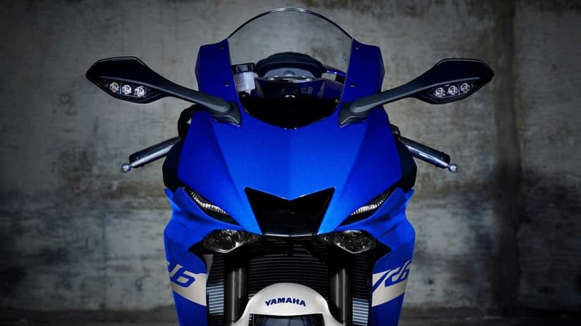 Front view of a blue Yamaha R6 sportbike with LED lights and mirrors against a textured concrete wall.