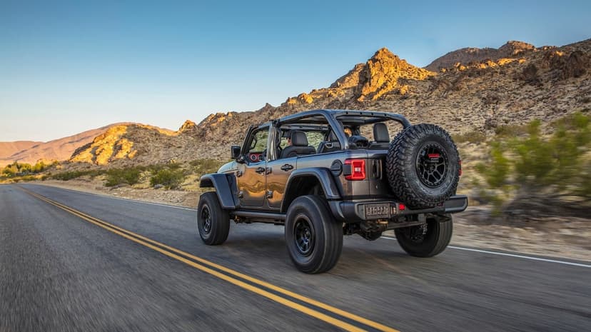 Jeep Wrangler Rubicon driving on a desert highway toward rocky mountains during a golden hour sunset scene.