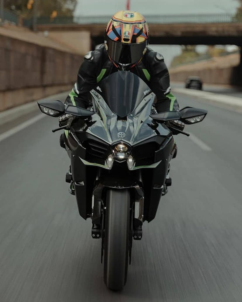 Motorcyclist in a black leather suit and colorful helmet riding a black sportbike on an open asphalt highway.