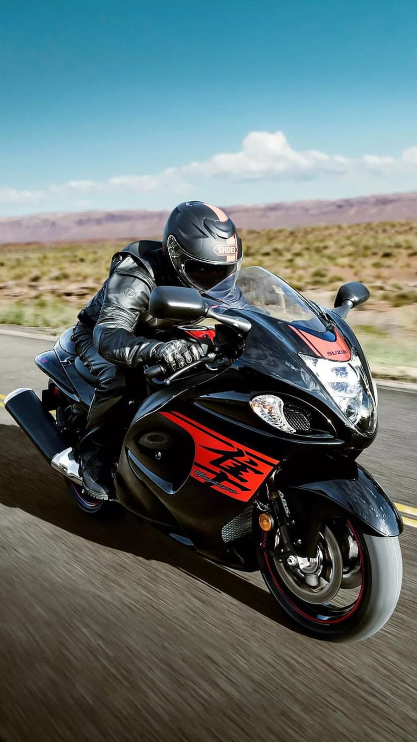Suzuki Hayabusa rider in black leathers speeding on a desert road under a blue sky with distant mountains.