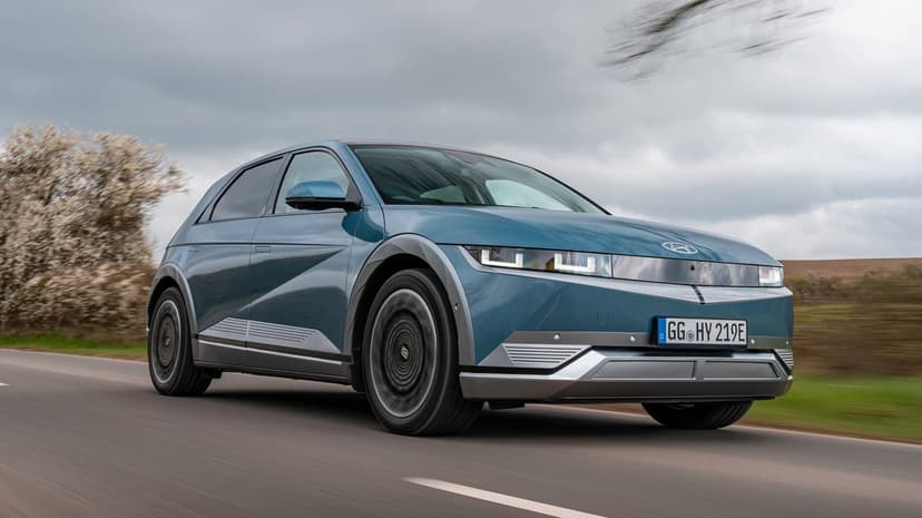 Blue Hyundai IONIQ 5 electric car driving on a road under a cloudy sky with motion blur on the wheels.