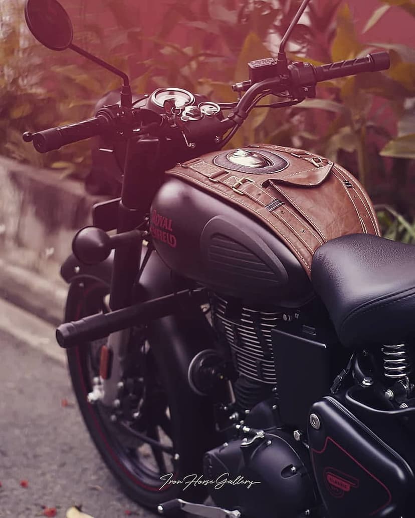 Royal Enfield bike with a brown leather tank cover, buckle straps, and chrome engine parts in a close-up shot.