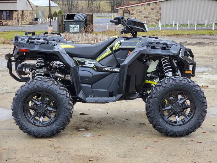 Black and lime green Polaris Sportsman ATV side view with aggressive off-road tires and white shock absorbers.