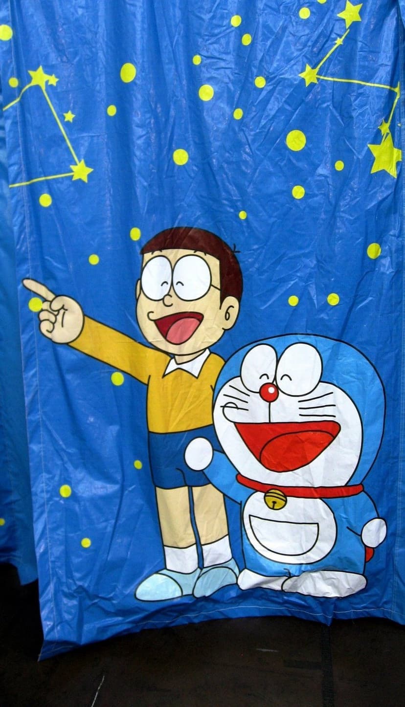 Doraemon and Nobita point at yellow stars and constellations on a textured blue background under a night sky.