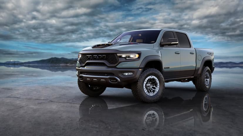 Slate gray Ram 1500 TRX pickup truck parked on a reflective surface under a dramatic cloudy sky with mountains.