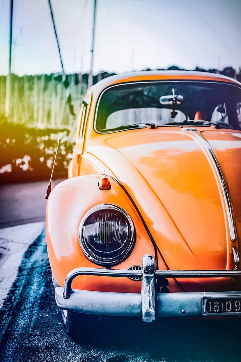 Orange vintage Volkswagen Beetle front view featuring a round headlight and chrome bumper on a wet road.