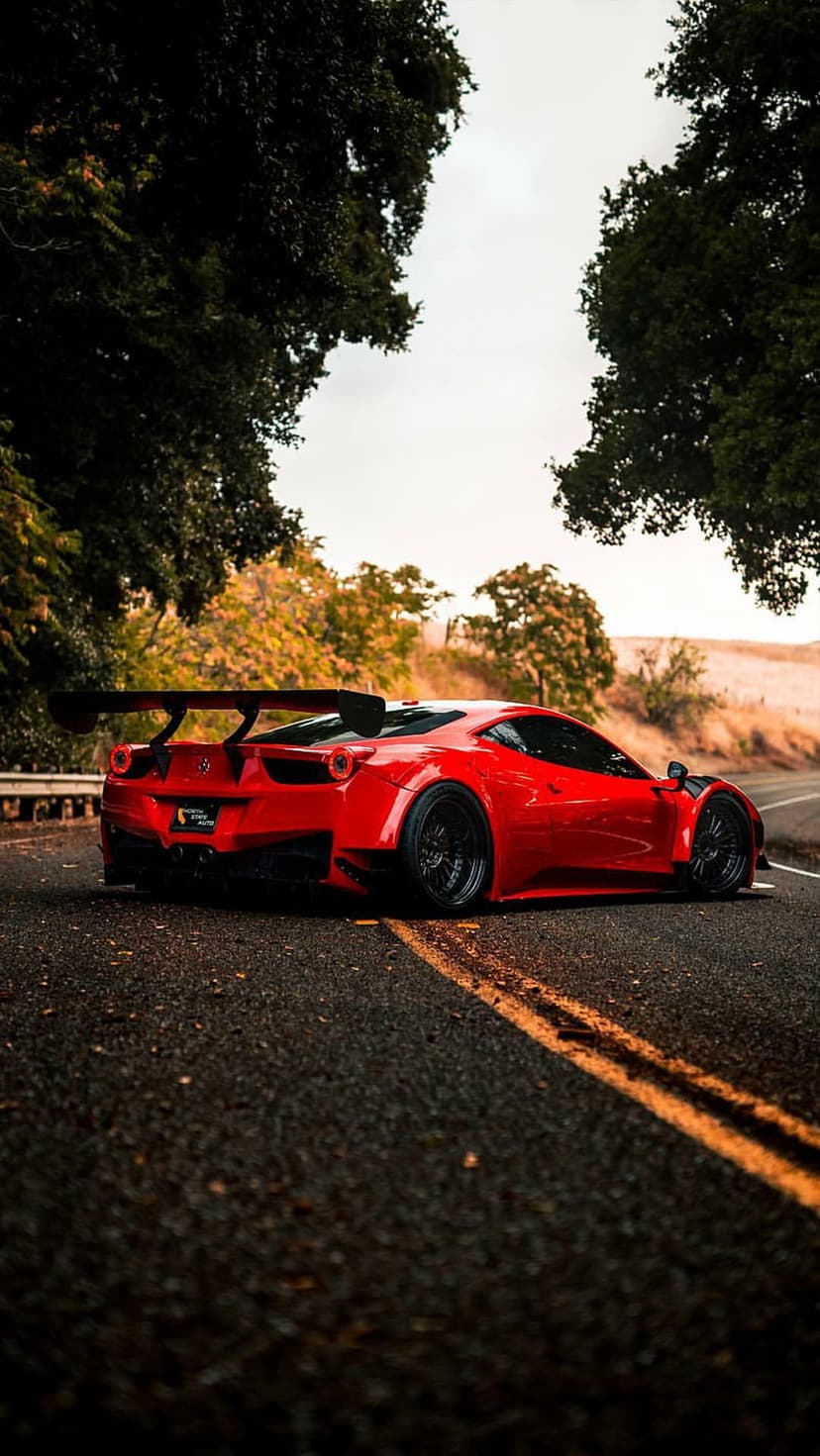 Red Ferrari 458 Italia sports car with a large rear wing parked on an autumnal road under warm light.