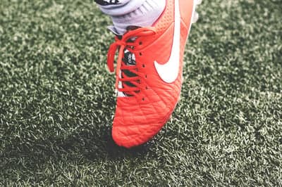 Close-up of a bright orange Nike soccer cleat on artificial turf