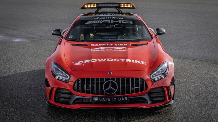 Front view of a red Mercedes-AMG GT R safety car with amber roof lights on an asphalt track background.
