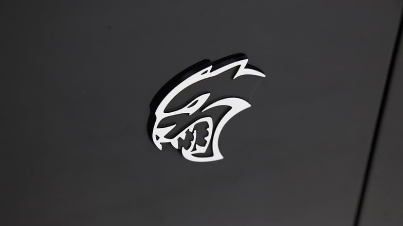 White Dodge Hellcat logo centered on a dark matte grey surface with subtle shadows and clean lines.