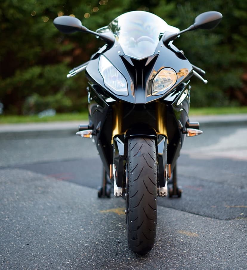 Black sport motorcycle front view with gold forks and LED headlights parked on an asphalt road with soft bokeh.
