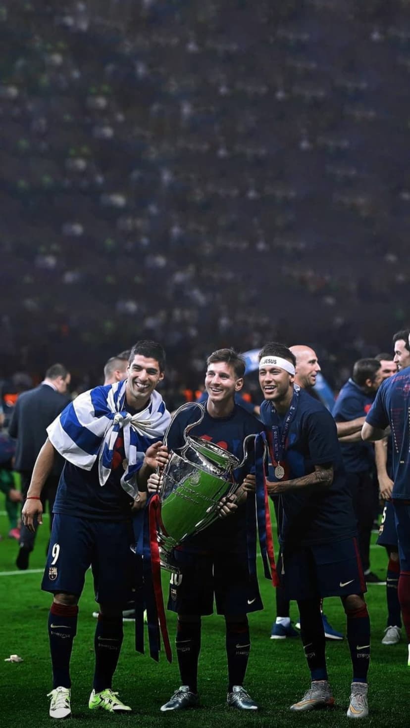 Messi, Suárez, and Neymar hold a large gold trophy while wearing striped Barcelona jerseys in a packed stadium.