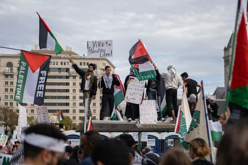Palestinian flags and a Viva Palestina Libre sign held by a crowd of protesters near an urban building.