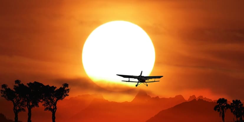 Biplane silhouette flying in front of an enormous orange sun above dark rolling hills and scattered trees.