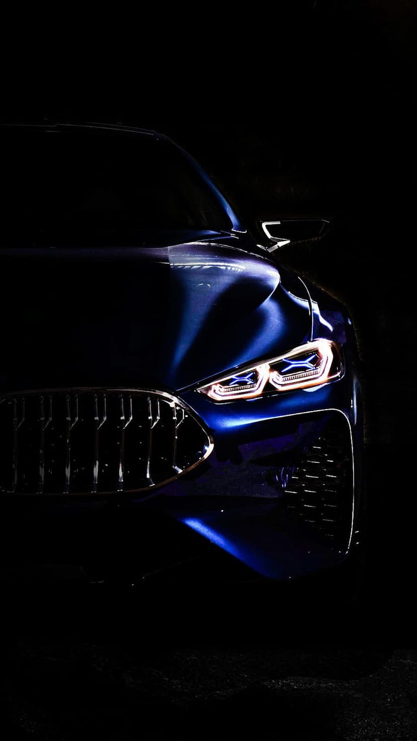 BMW front grille and glowing LED headlights illuminate a dark night scene with sharp blue metallic reflections.