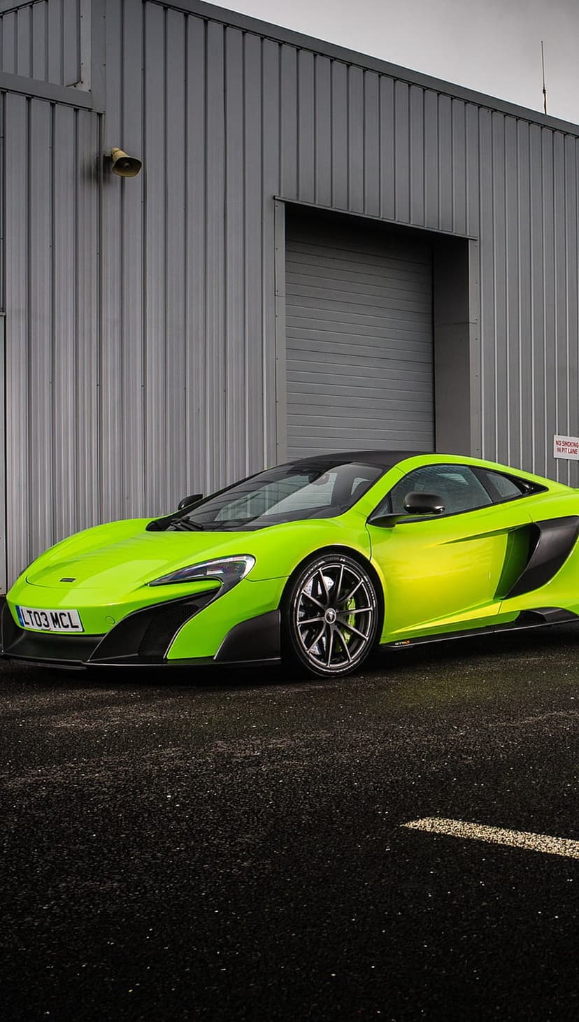 Lime green McLaren 675LT supercar parked on wet asphalt with its black roof reflecting on the slick road surface.