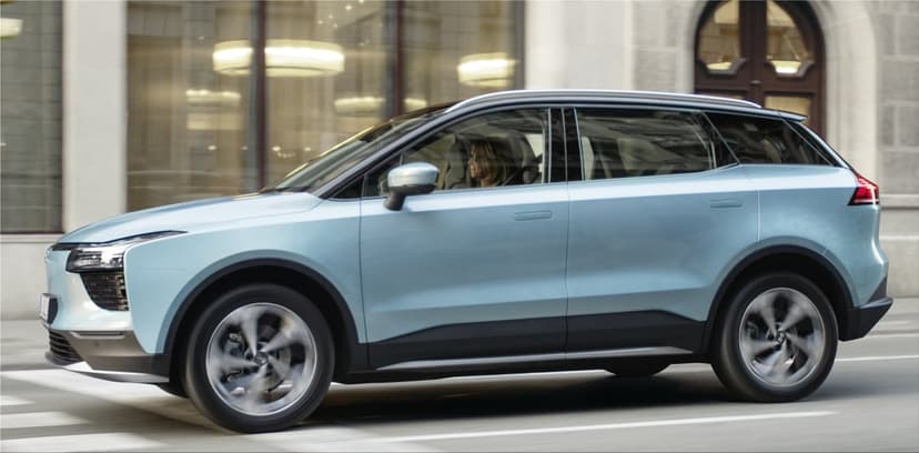 Light blue electric SUV driving on a city street with motion blurred wheels and architectural reflections.