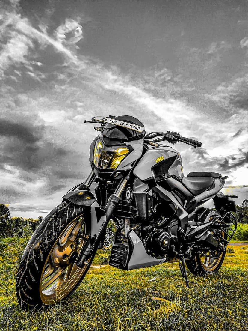 Black sportbike with amber headlights and golden rims rests on green grass under a dark overcast sky.