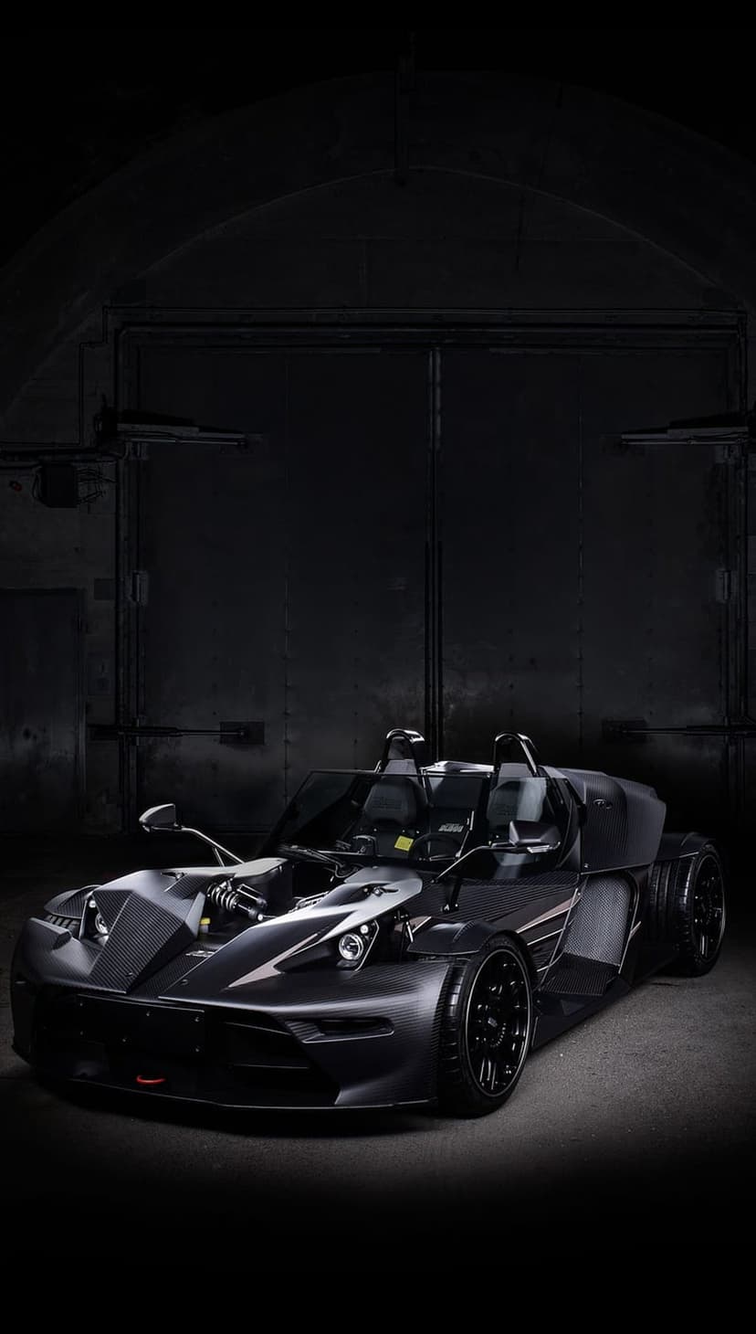 Matte black sports car with exposed engine parts in a dark industrial garage with dramatic lighting and shadows.