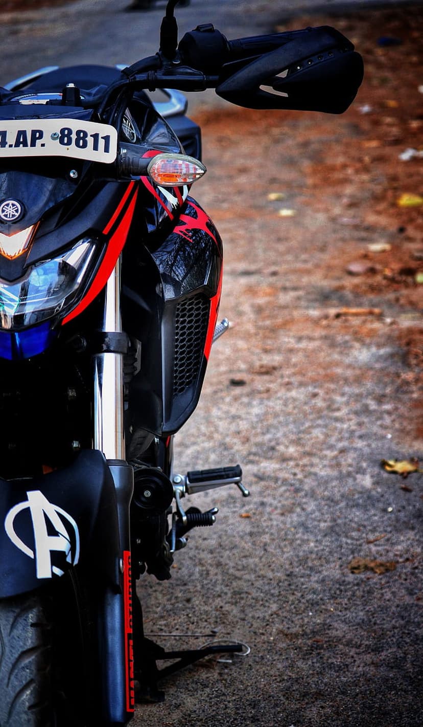 Black Yamaha motorcycle front with LED headlights, red stripes, and Avengers logo on a textured ground.