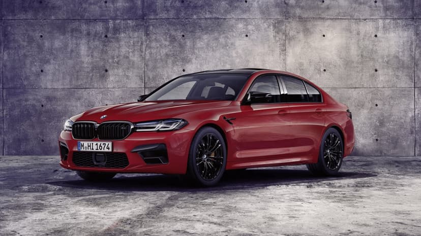 Red luxury sports sedan parked in front of a textured concrete wall with black wheels and aggressive styling.