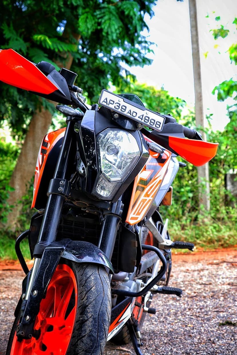 KTM Duke motorcycle with a bright orange rim and sharp LED headlight parked on a blurred outdoor nature trail.
