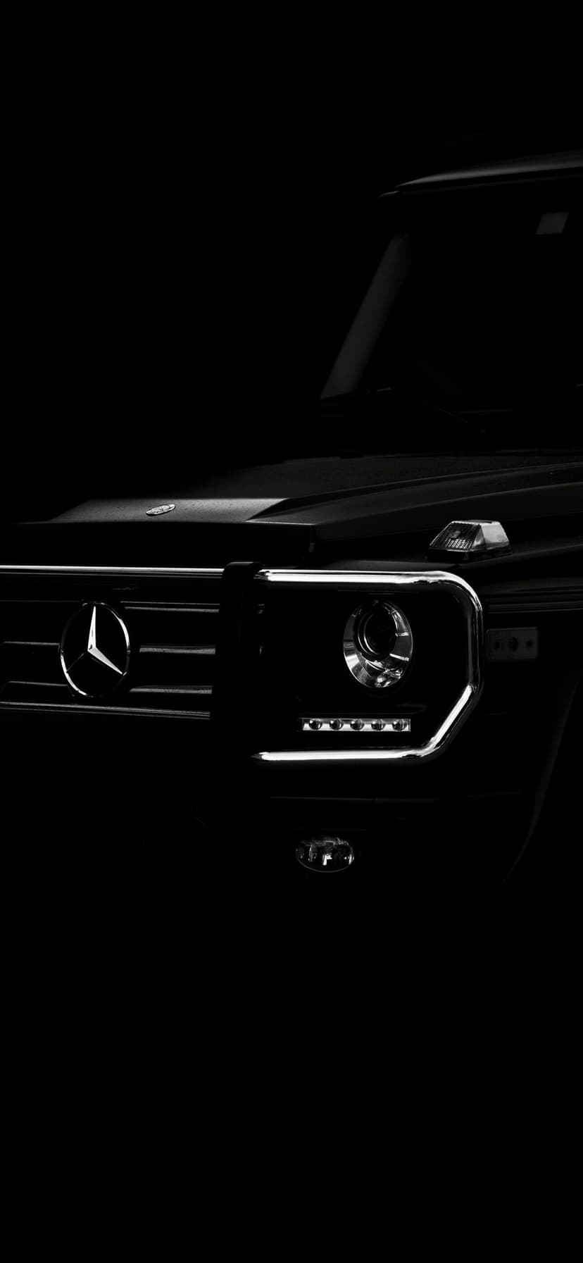 Front profile of a black Mercedes G-Wagon with glowing LED headlights in deep shadow chiaroscuro lighting.