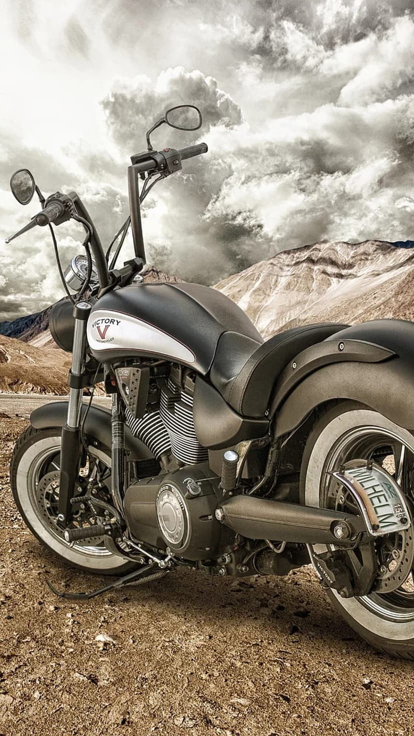 Victory cruiser motorcycle with chrome accents parked on a rocky plateau beneath a dramatic mountain sky.