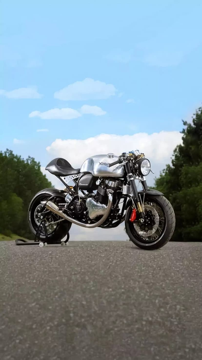 Norton cafe racer motorcycle with a chrome tank on an asphalt road with green trees under a blue sky.