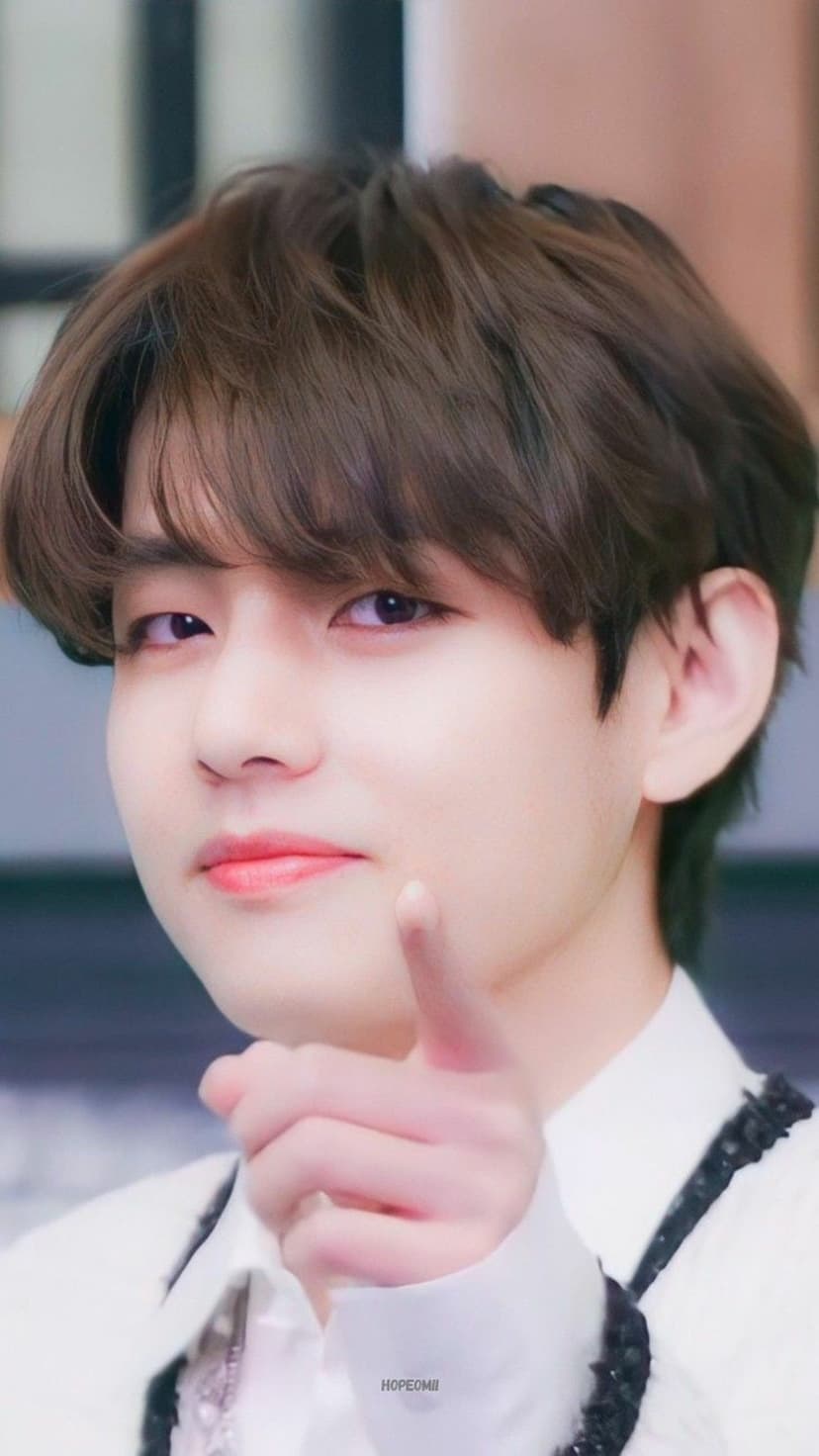 Kim Taehyung points his index finger toward the viewer while gazing forward in this warm close-up portrait.