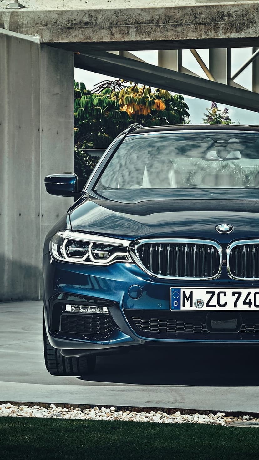 Dark blue BMW 5 Series wagon featuring LED headlights and a chrome grille inside a modern concrete parking garage.