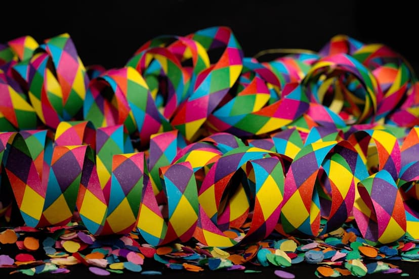 Multicolored paper streamers with diamond prints and circular confetti scatter over a pitch-black surface.
