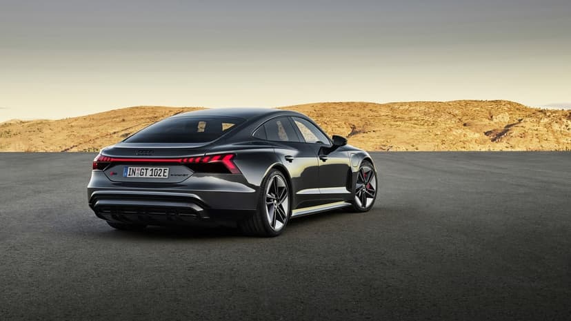 Dark grey Audi RS e-tron GT with red LED taillights parked on asphalt against a desert hill backdrop.