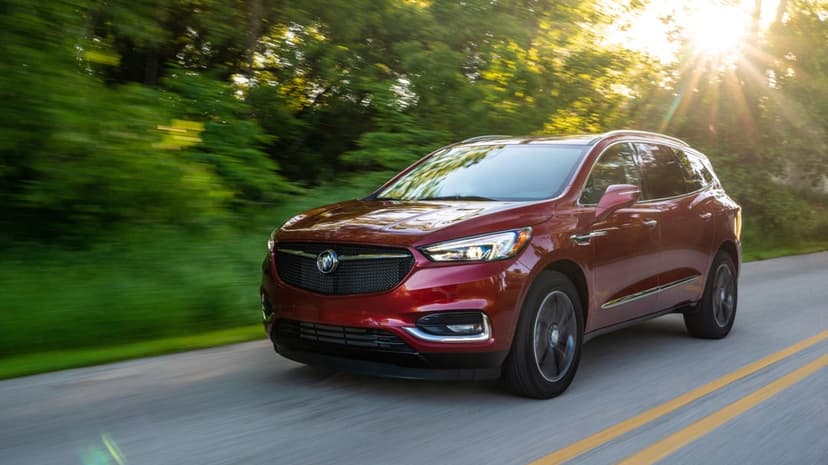 A maroon Buick SUV driving on a scenic forest road with golden sun rays piercing through motion blurred green trees.