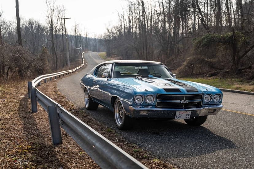 Light blue 1970 Chevrolet Chevelle SS with black stripes on a winding road through a leafless forest.