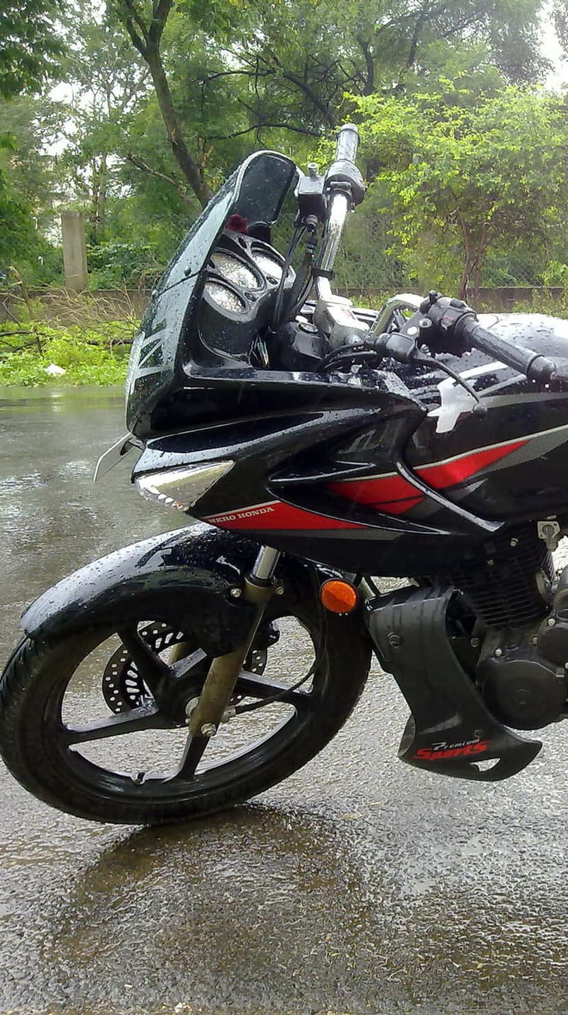 Black sportbike with red accents and raindrops on the fairing parked on a wet reflective surface near green trees