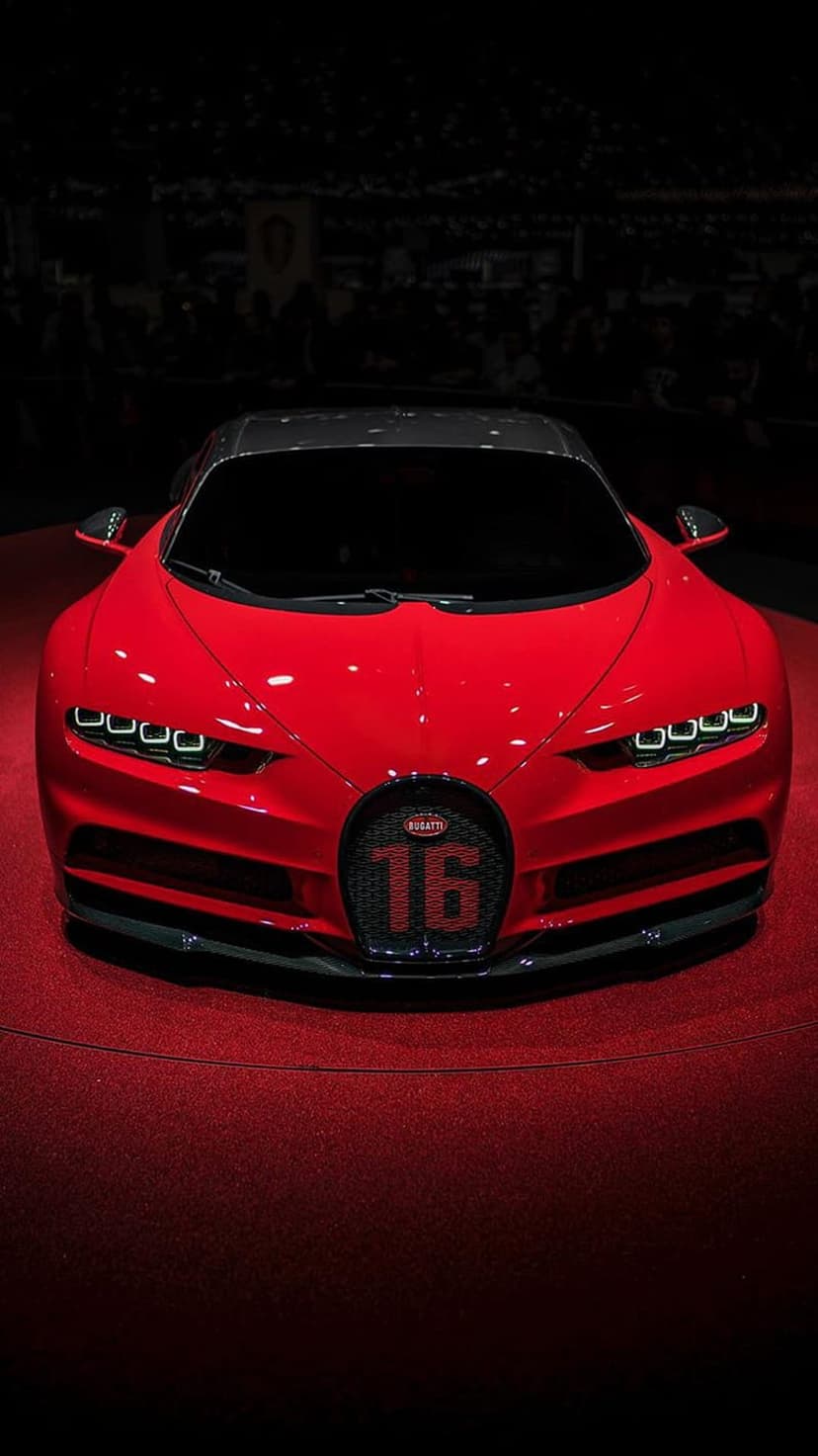 Red Bugatti Chiron hypercar with number 16 on the grille parked on a red carpet under dramatic studio lighting.