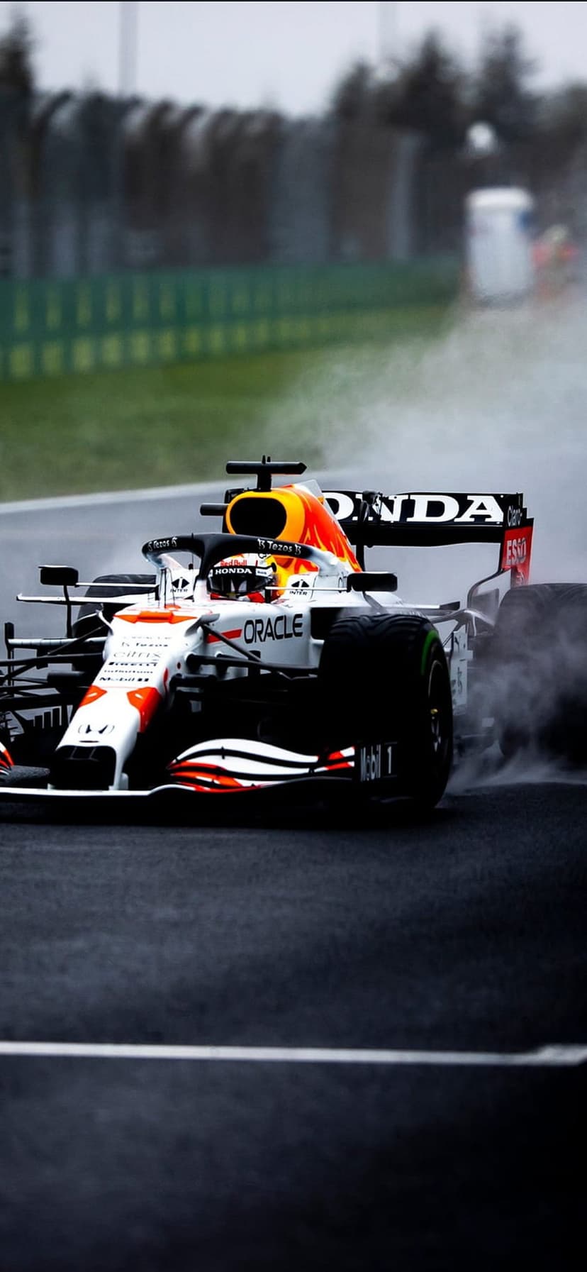 Red Bull Racing F1 car speeds through rain on a wet track with misty water spray trailing from rear tires.