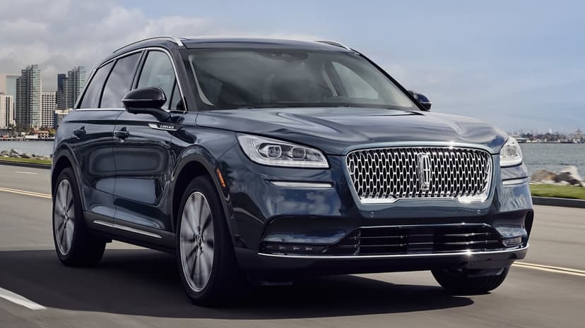 Dark blue Lincoln Corsair SUV driving on a coastal road with a city skyline and ocean in the background.