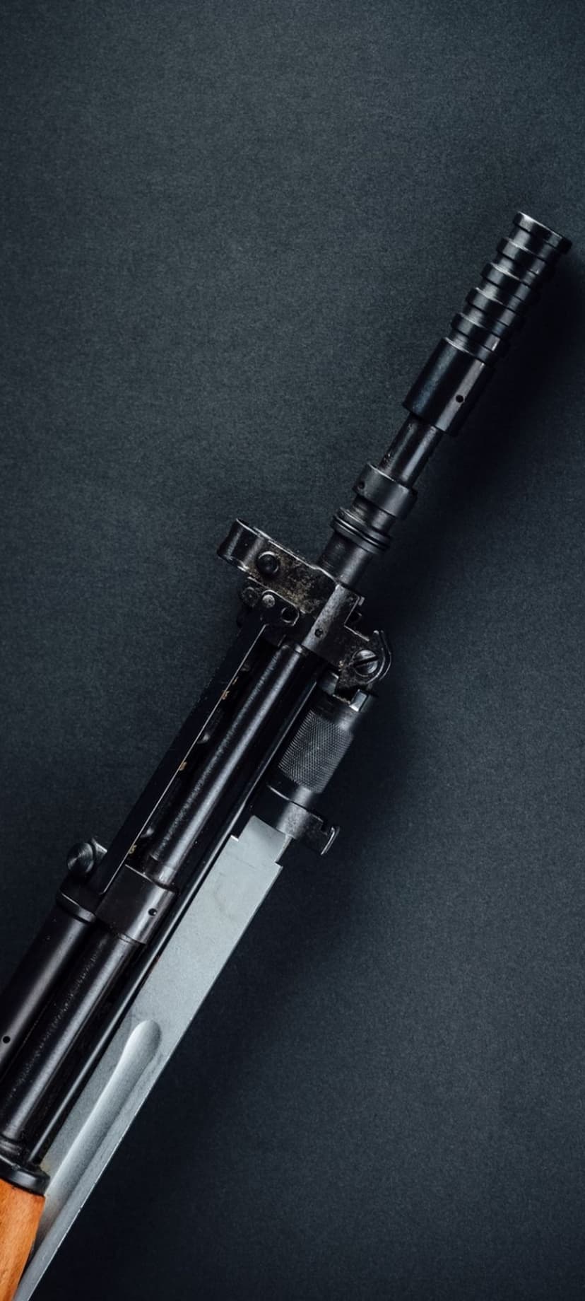 AK-47 rifle barrel and fixed bayonet blade with cold metallic textures against a dark, moody background.