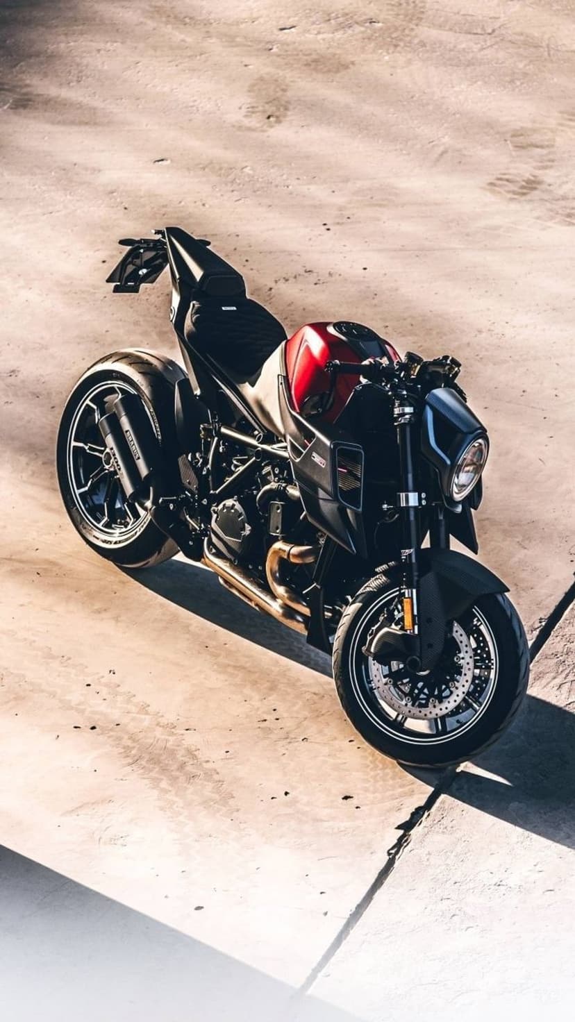 Red and black sportbike parked on textured concrete with long shadows cast by sunlight in a high-angle view.
